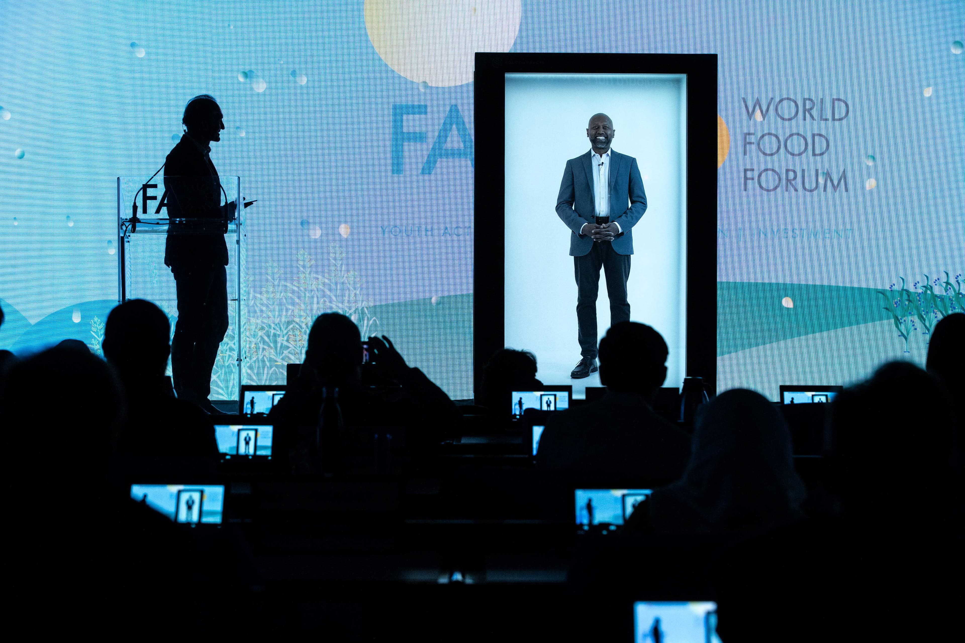 A keynote speaker appearing as a life-size hologram at the World Food Forum, while a moderator on stage interacts with the audience.